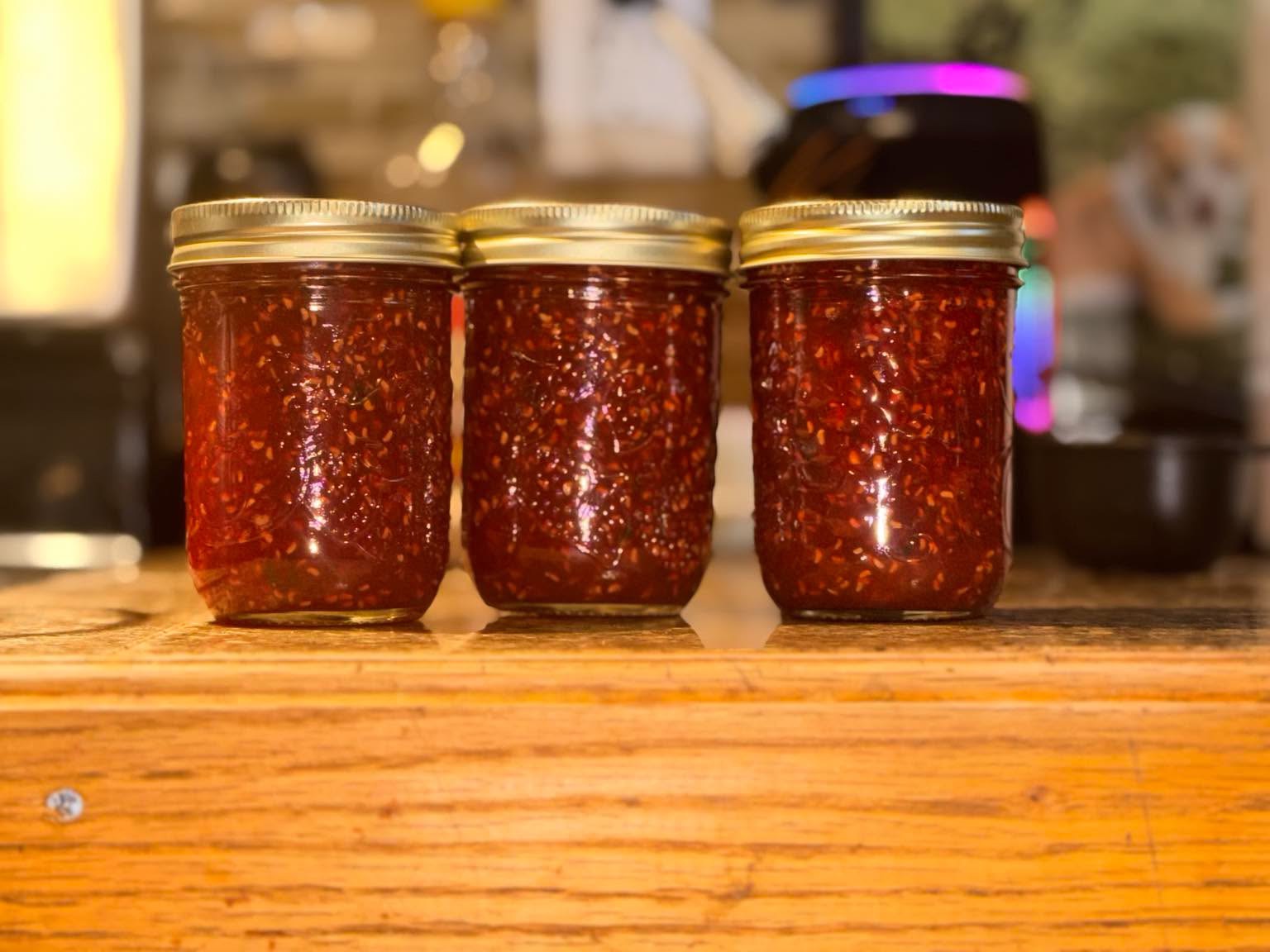 Three jars of seeded red preserves on a wooden counter